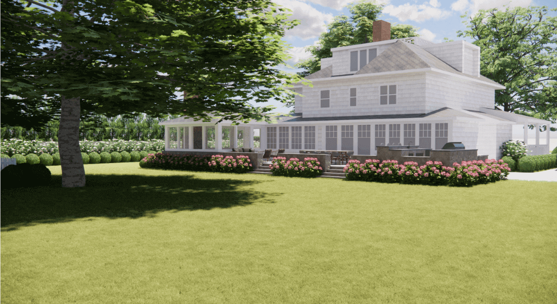 A white two-story house with a porch and outdoor deck is surrounded by green lawn, trees, and flower bushes under a partly cloudy sky.